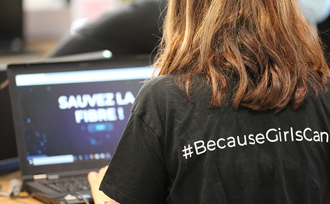 Femme de dos sur un ordinateur portant un tshirt #becausegirlscan